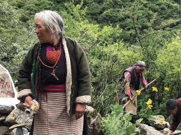 Respekt vor der Natur: Eine ältere Frau und die Sorge um Tibets Landschaft Eine alte Frau in traditioneller tibetischer Kleidung hält eine leere Getränkedose, ein Zeichen für Umweltbewusstsein im ländlichen Tibet.