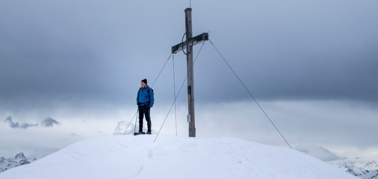 Oliver Jackson steht mit Schneeschuhen am Gipfelkreuz des Portlahorns.