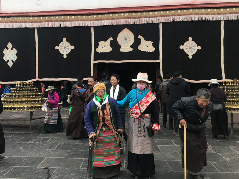Tradition und Respekt: Das hohe Ansehen Älterer in Tibet Tibetische Senioren, gekleidet in farbenfrohe traditionelle Gewänder, vor einem heiligen Ort, ein Spiegelbild der kulturellen Wertschätzung für das Alter.